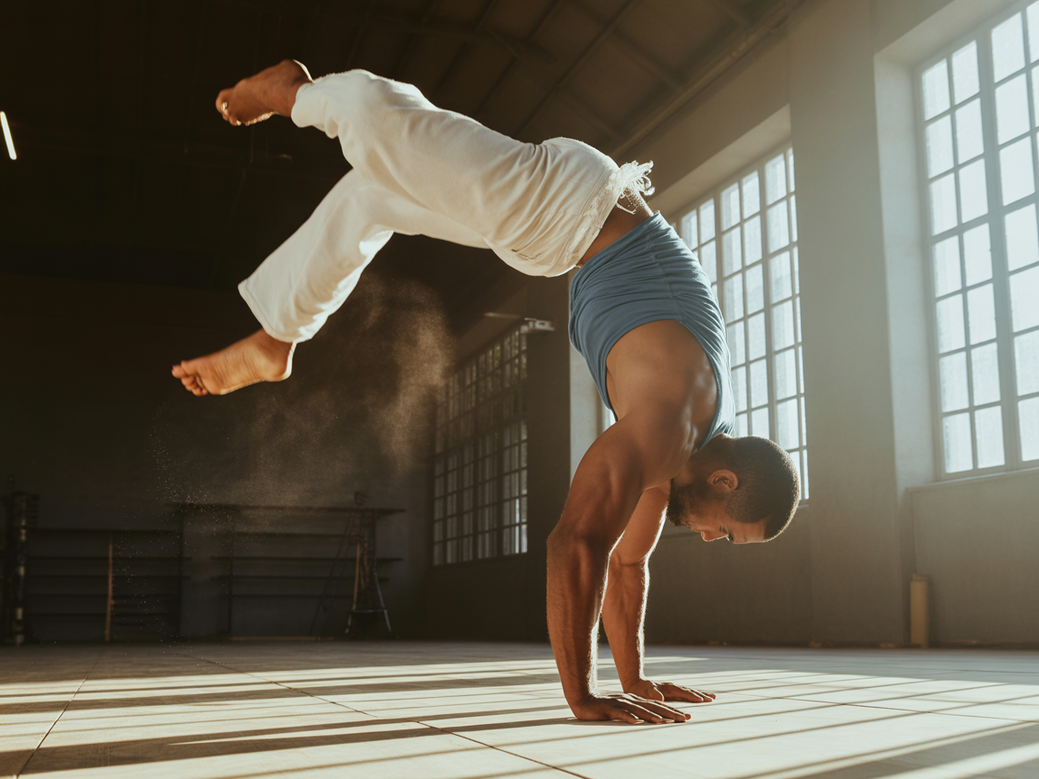 Capoeirista executando um movimento de chão que demonstra a importância de fortalecer ombros para capoeira, com a musculatura em destaque.