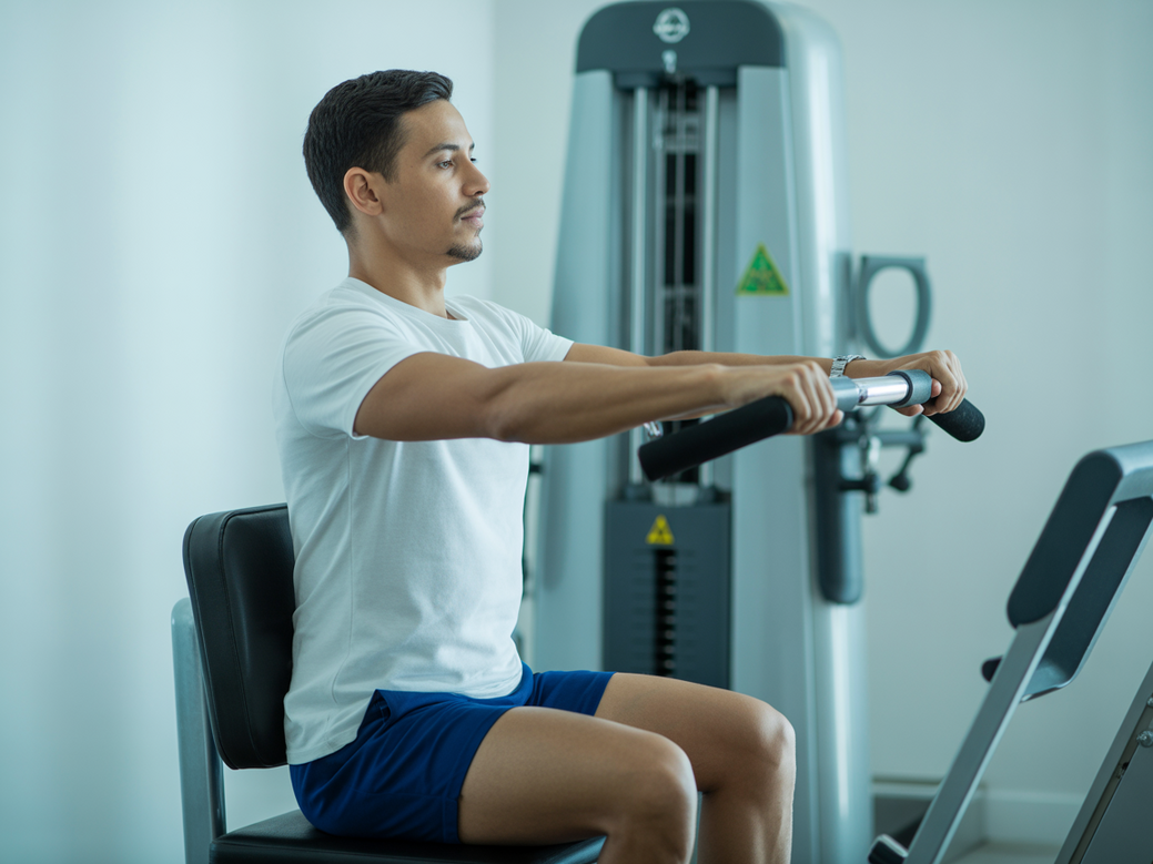 Paciente realizando elevação lateral na máquina como parte do treino de ombro na máquina pós-covid.