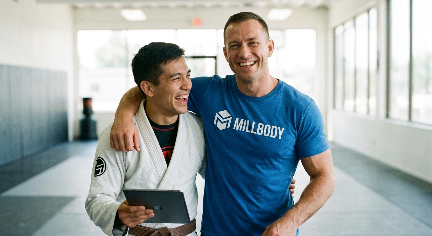 Personal trainer vegano com camiseta Millbody ao lado de aluno de Jiu-Jitsu segurando tablet
