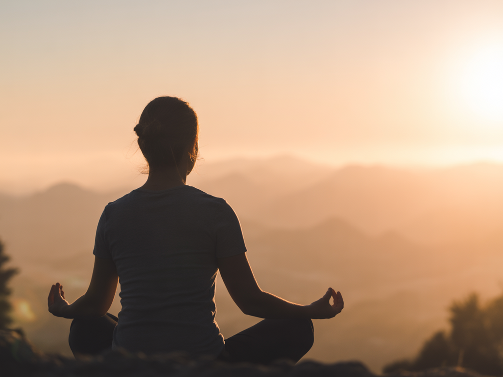 A person practicing yoga for anxiety with meditation at sunrise.